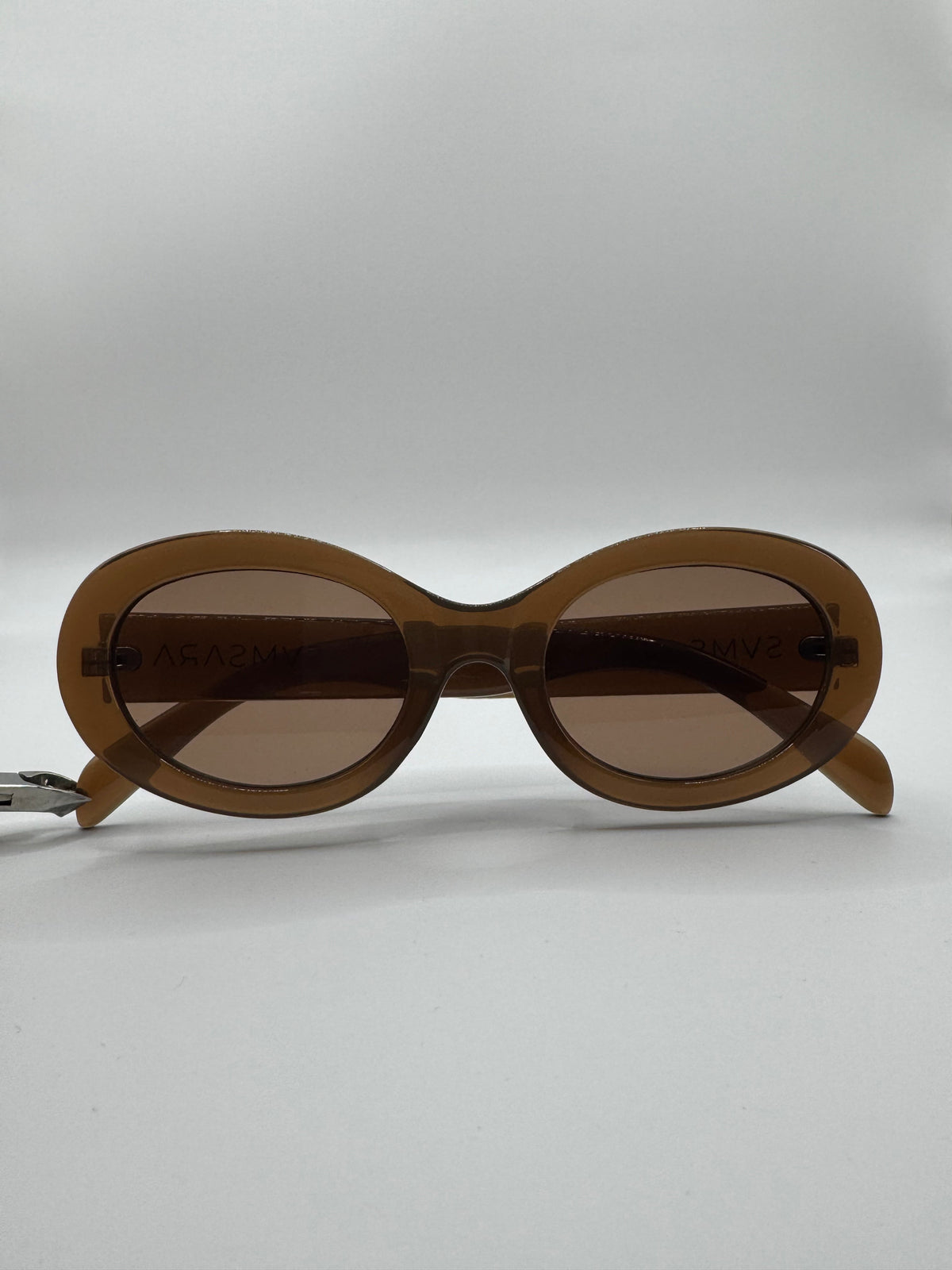 Gafas de sol ovaladas de montura marrón translúcida fotografiadas de frente sobre fondo blanco