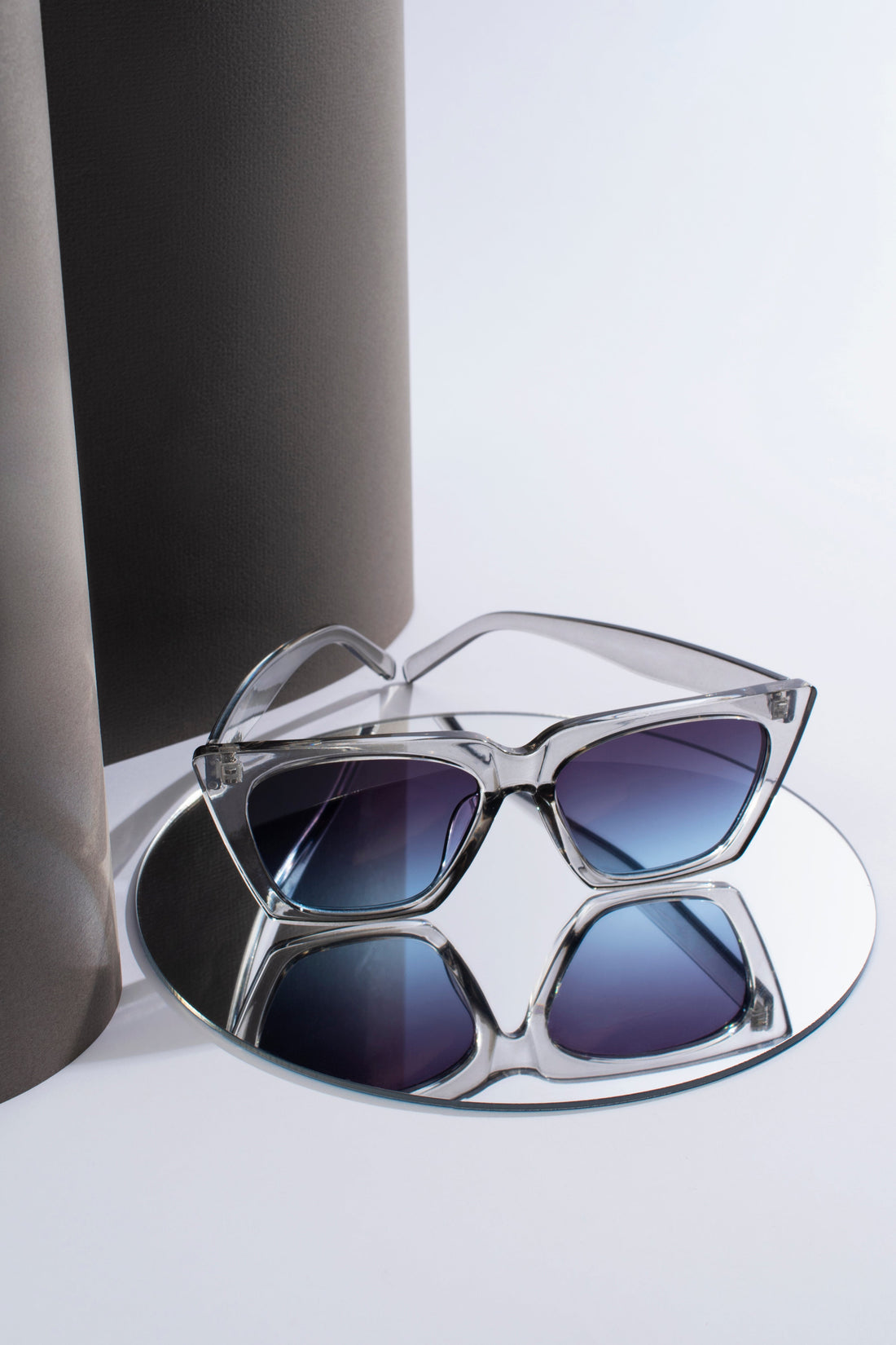 Gafas de sol de montura transparente con lentes degradadas azules sobre una superficie reflectante