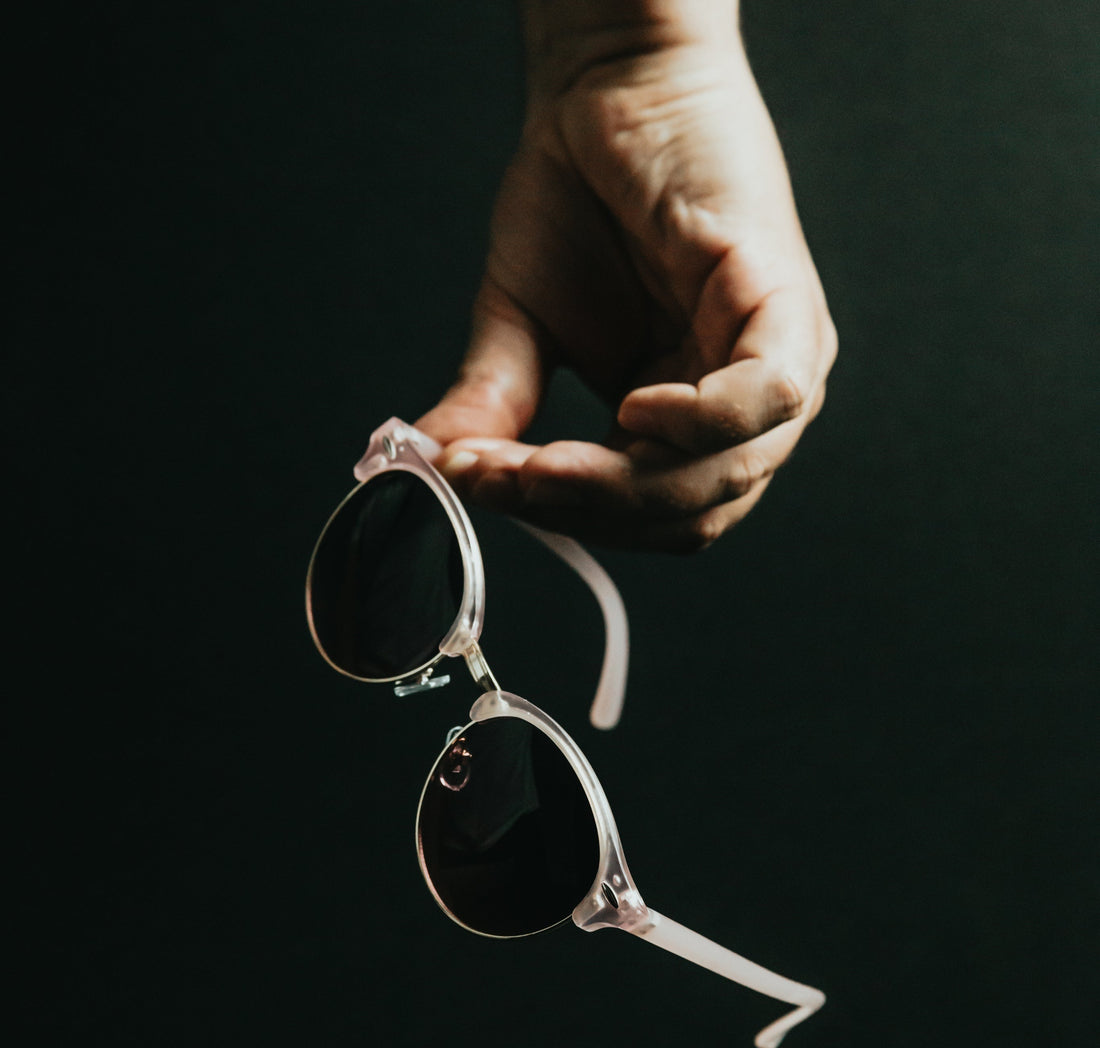 Mano sujeta una montura de gafas translúcida sobre un fondo oscuro