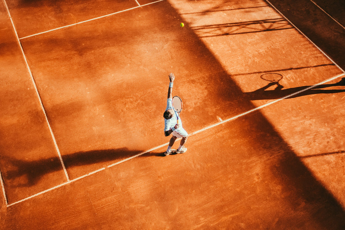 Jugador de tenis en una pista de tierra batida durante el saque, visto desde arriba