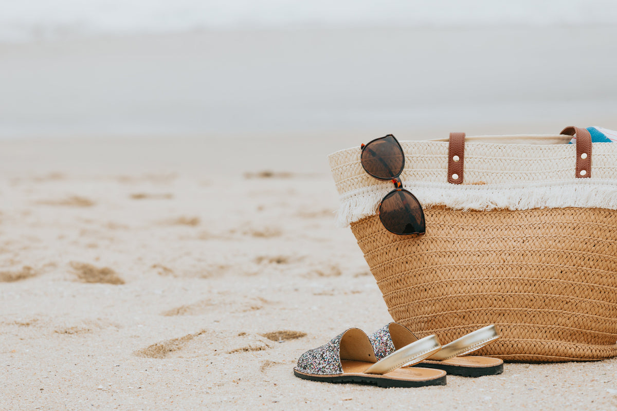 Gafas de sol oscuras colgadas de un bolso de playa junto a la arena