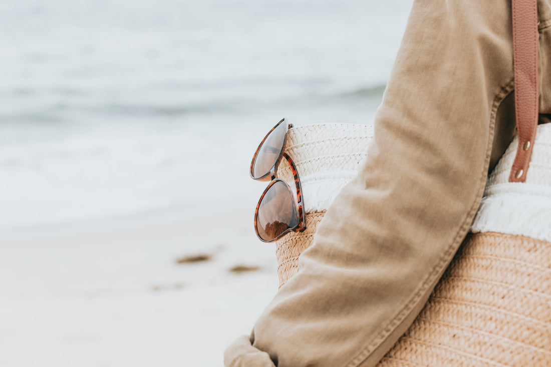 Gafas de sol carey colgadas de un bolso de playa tejido junto al mar