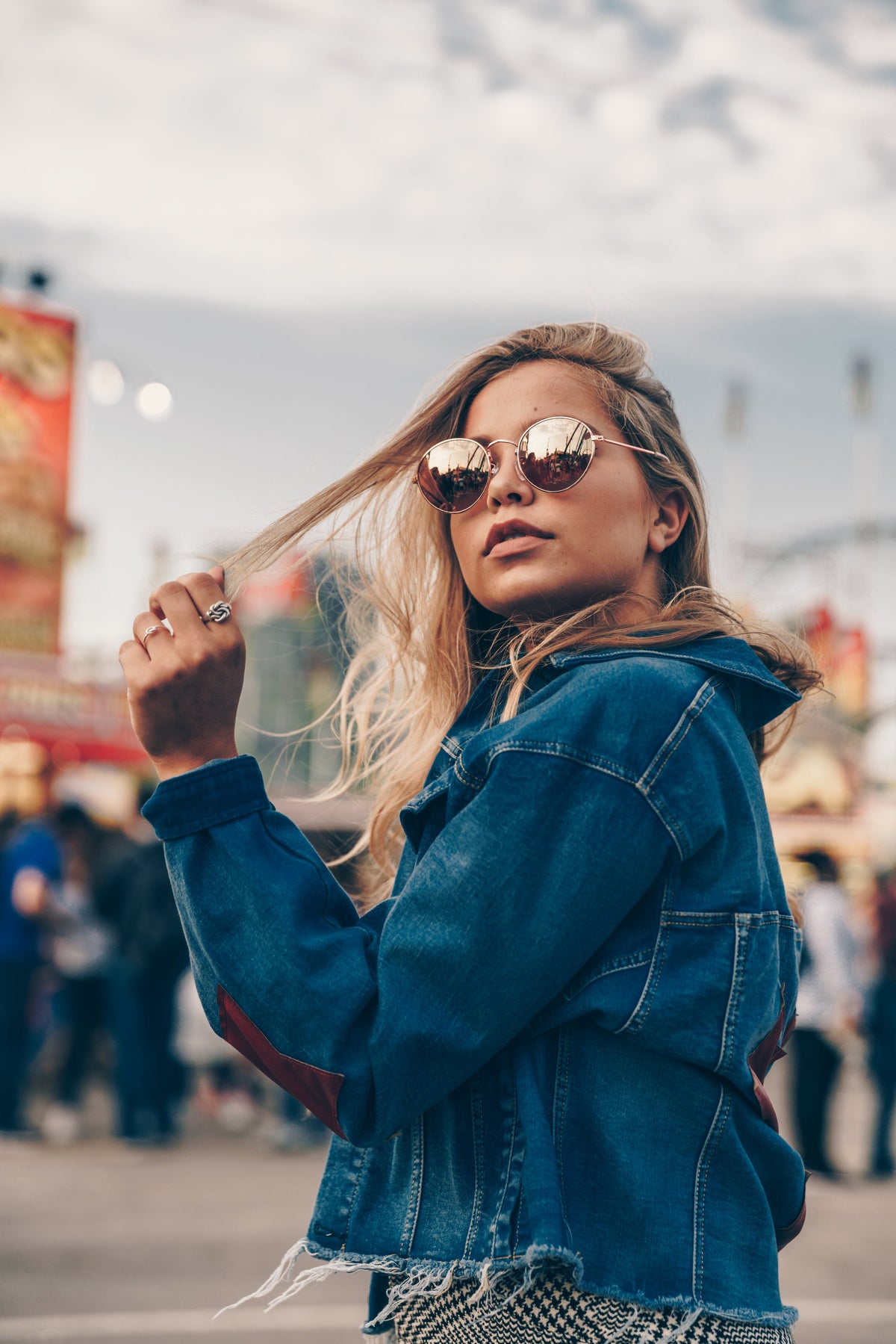Mujer con gafas de sol de lentes redondas reflectantes y chaqueta vaquera en un entorno exterior